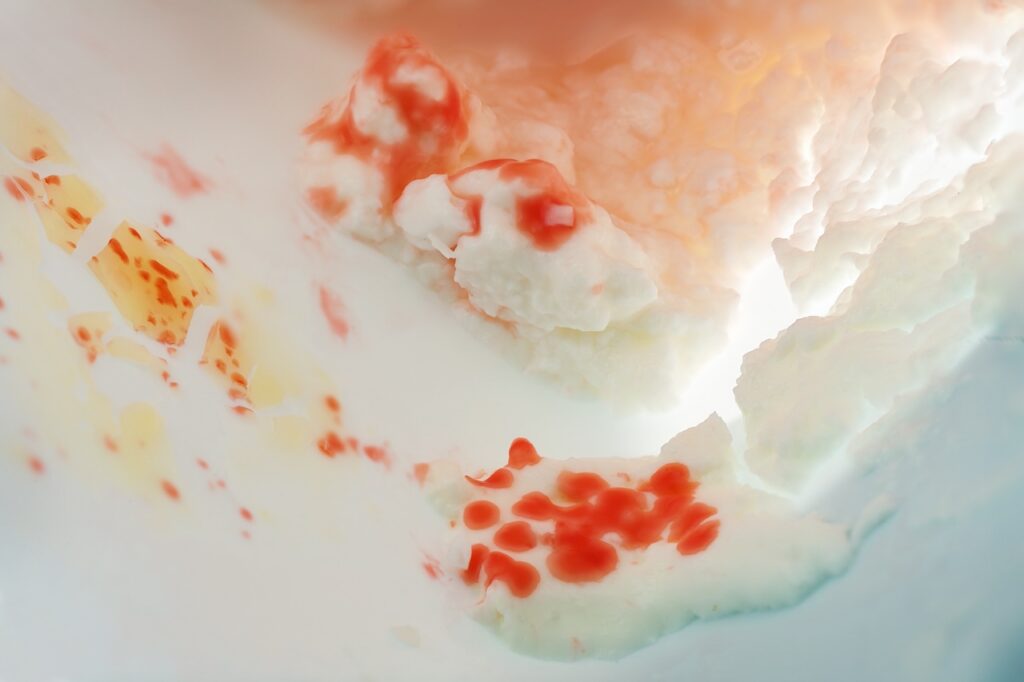 Serratia marcescens, rod-shaped bacteria with red pigment growing in a package of curd cheese, probably due to contamination during filling, concept for health care, hygiene and preventing food spoilage, copy space, abstract macro shot with selected soft focus