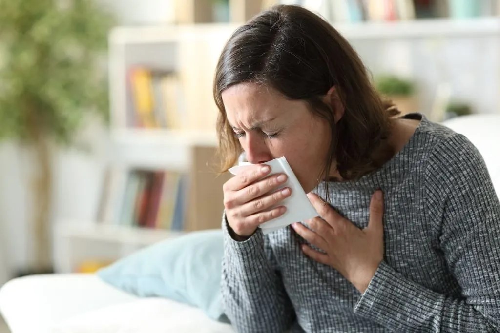 A woman sneezing into a tissue.