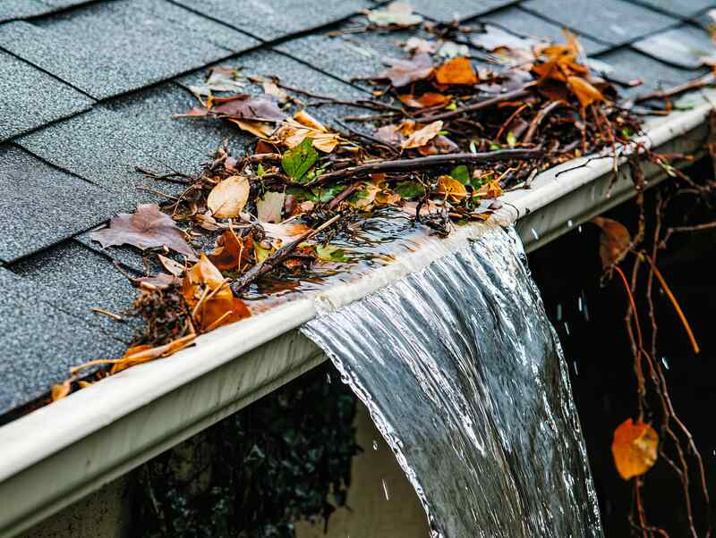 Overflowing gutter clogged with leaves causing water damage risk during winter storms.