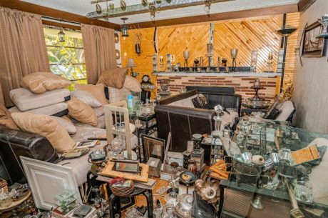 Cluttered living room filled with stacked furniture, pillows, glassware, and various household items, illustrating a severe hoarding situation. Dangers of Hoarding