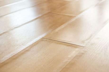A close-up view of a light-colored laminate floor with visible bubbling and warping, showing raised and uneven planks due to moisture damage or improper installation.