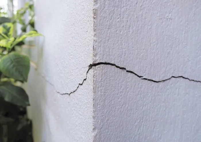 Horizontal foundation crack in exterior stucco wall – potential structural damage requiring inspection and restoration. Water damage on concrete