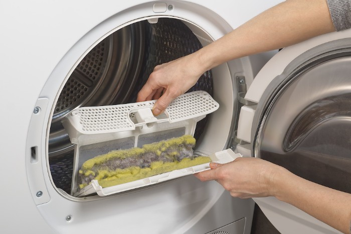 A person practicing good dryer fire prevention protocols and cleaning the lint trap