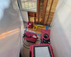 Dehumidifier and air movers positioned near exposed wall framing during drying