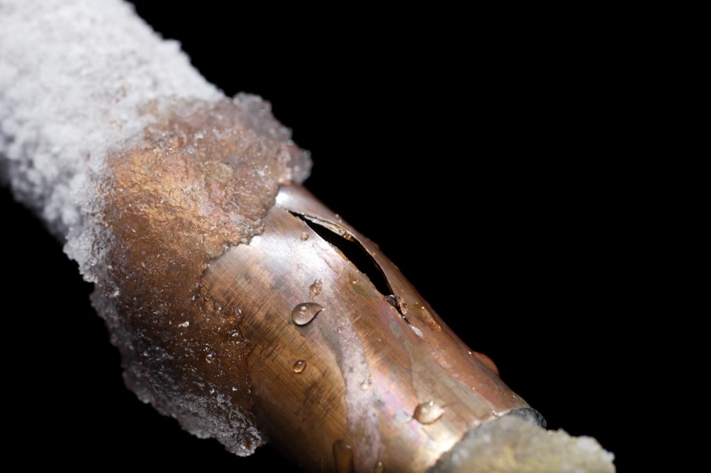 Close-up of a burst frozen copper pipe with ice and water damage risk on Long Island.