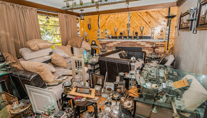 Cluttered living room filled with stacked furniture, pillows, glassware, and various household items, illustrating a severe hoarding situation. Dangers of Hoarding