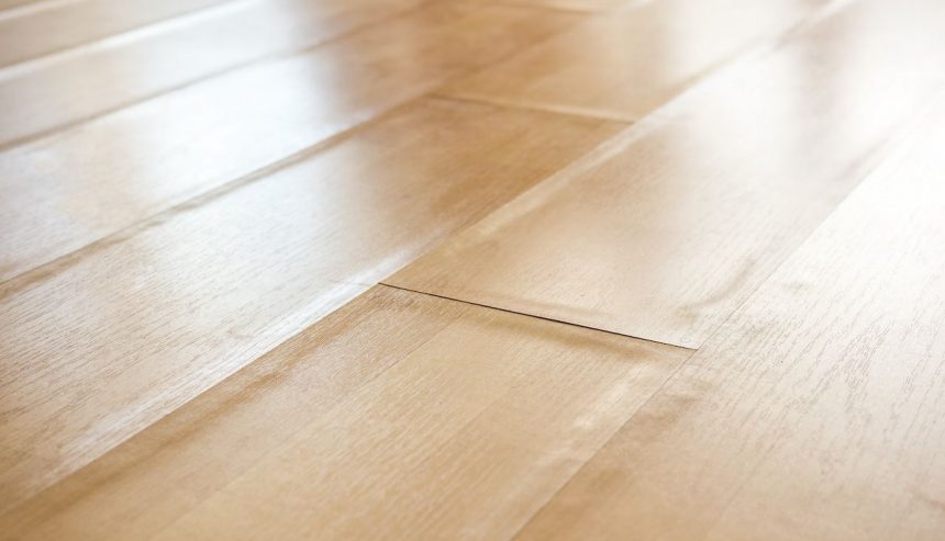 A close-up view of a light-colored laminate floor with visible bubbling and warping, showing raised and uneven planks due to moisture damage or improper installation.