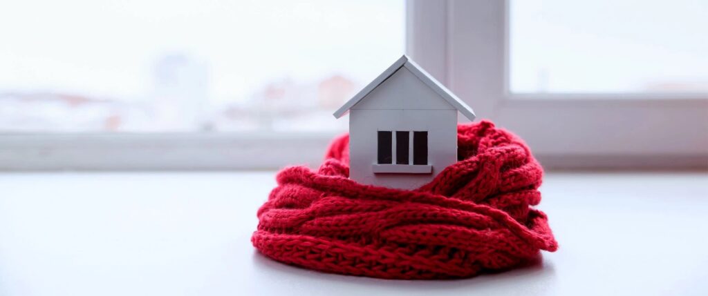 Miniature house wrapped in a red scarf symbolizing winter home protection on Long Island.