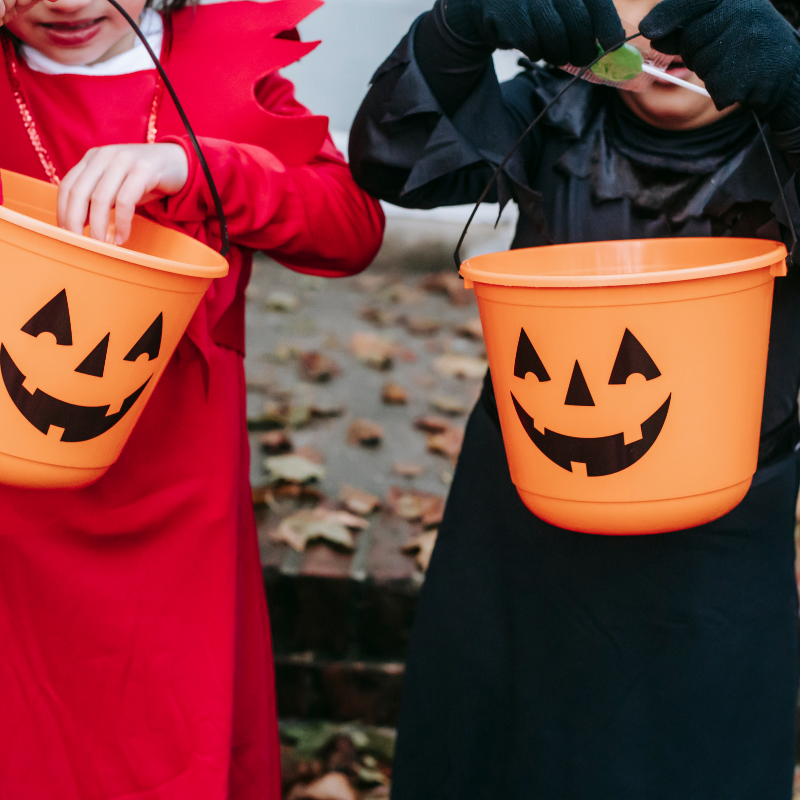 Two children in Halloween costumes hold jack-o'-lantern buckets while trick-or-