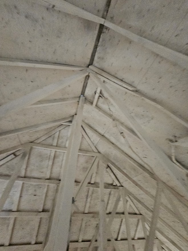 Light-colored wooden rafters and plywood create the geometric structure of an unfinished attic ceiling.