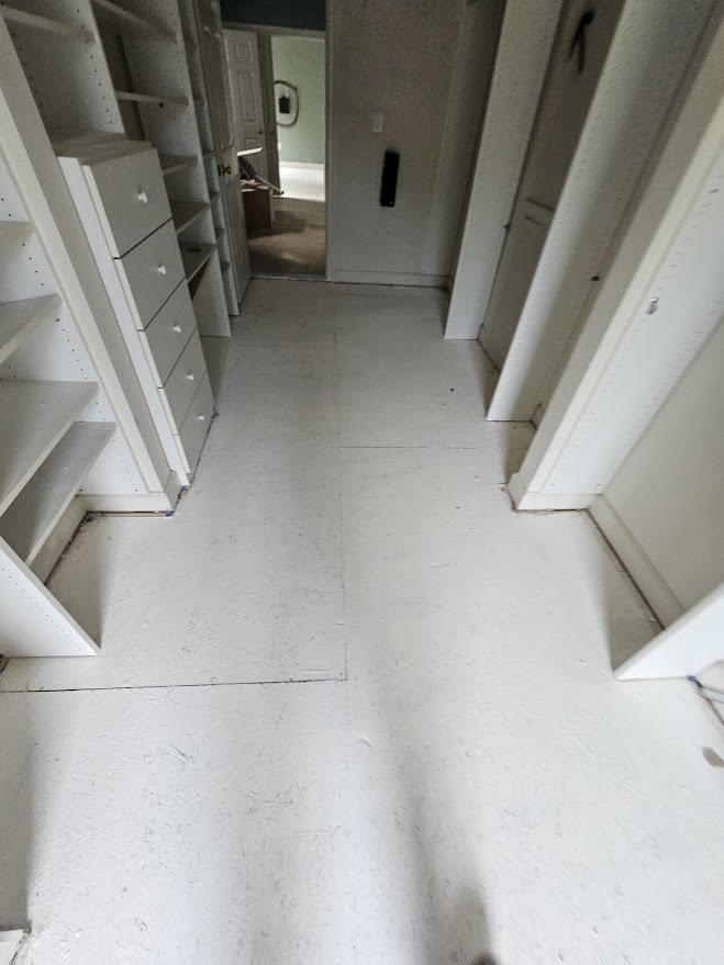 Empty walk-in closet featuring white built-in shelves, drawers, and a light-colored