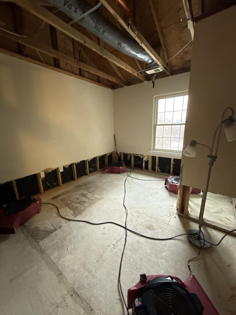 A room undergoing water damage restoration with exposed wall studs, ceiling beams, and multiple industrial drying fans