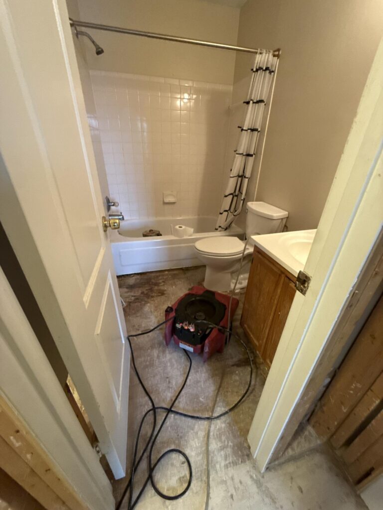 An industrial air mover dries the exposed subfloor in a bathroom undergoing water damage restoration. TITLE