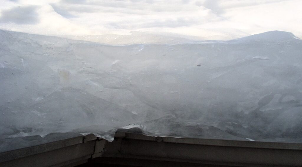 “Thick ice dam buildup along the roof edge, showing layered ice blocking proper drainage.”