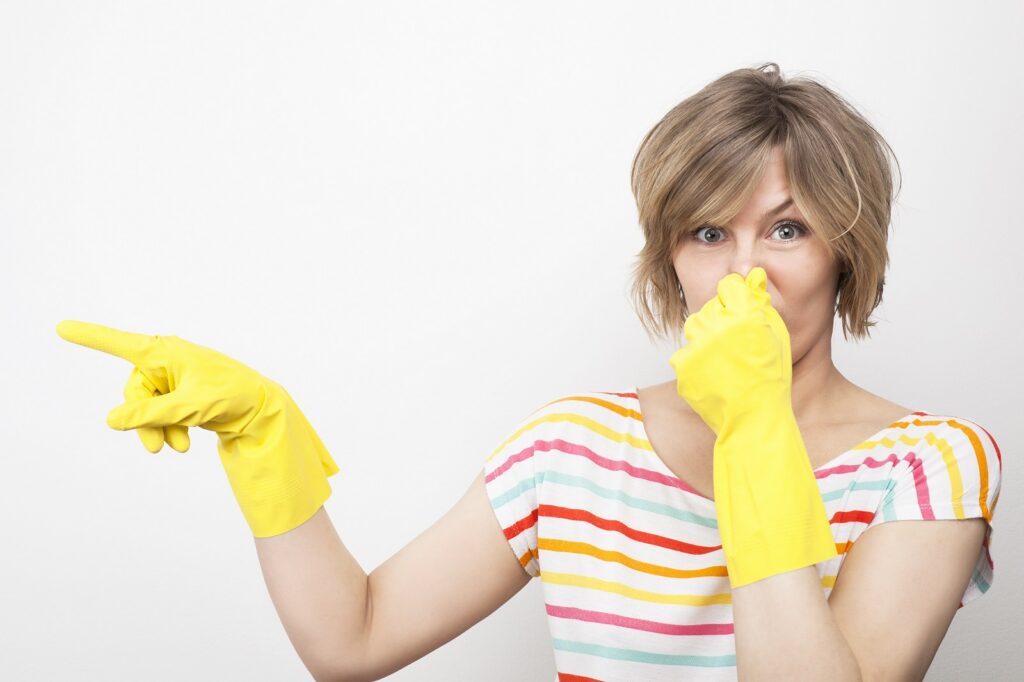 A woman covering her nose wearing yellow cleaning gloves