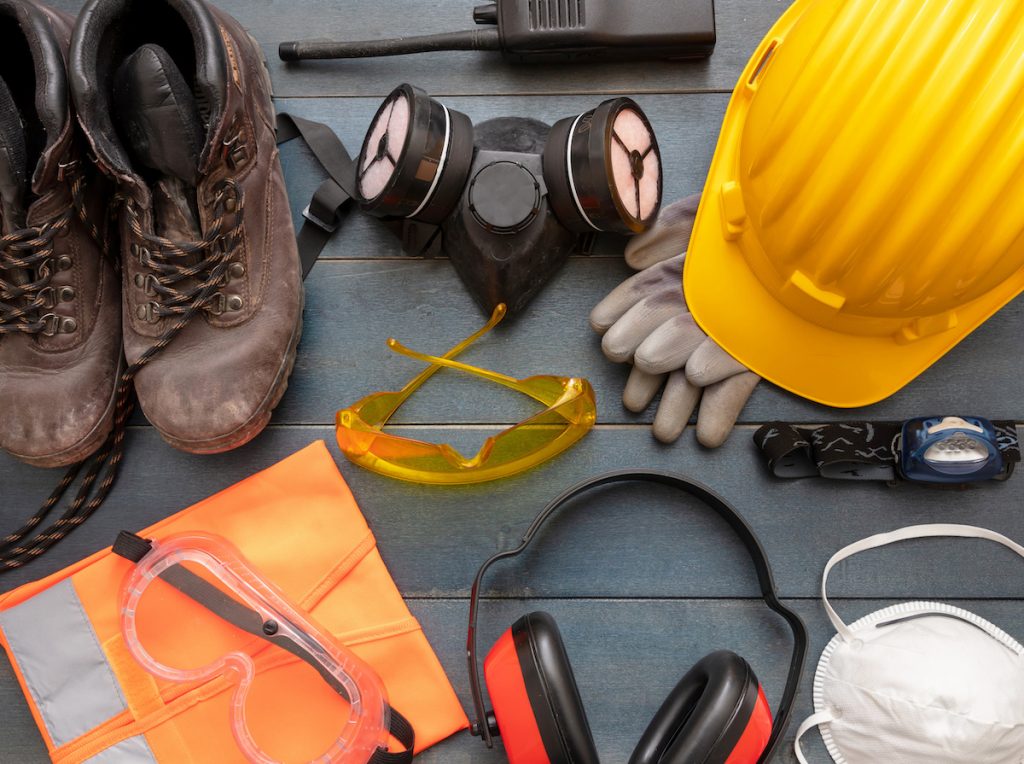 Work safety protection equipment. A hard hat, googles, a ventilation mask, headphones, work light, and work boots.