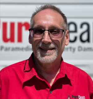 Greg Joyce from Puroclean smiling at the camera in front of a Puroclean work van