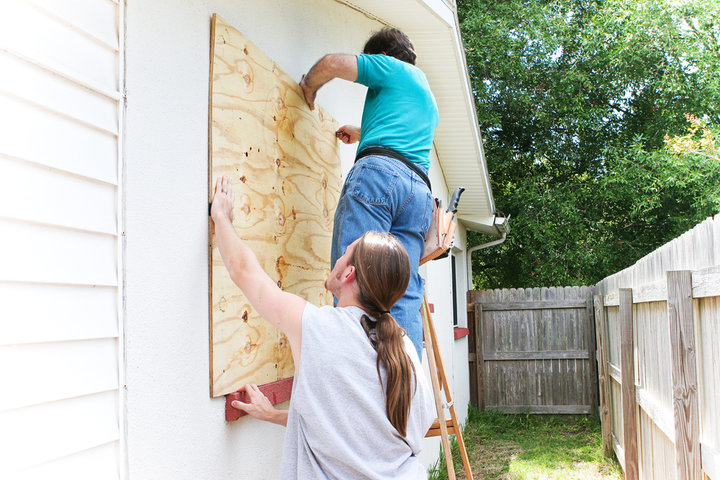 Two men bolting plywood over a window. 