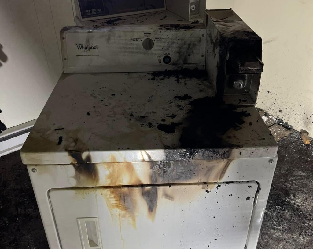A clothes dryer scorched and blackened by fire, with soot staining the control panel and front — the aftermath of a dryer fire that started in the vent