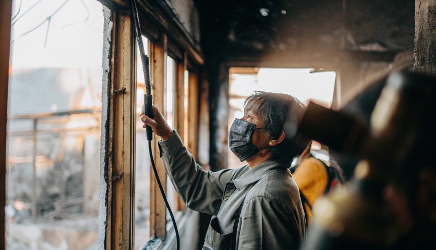 Person wearing a protective mask cleaning or inspecting a damaged building interior after a fire.