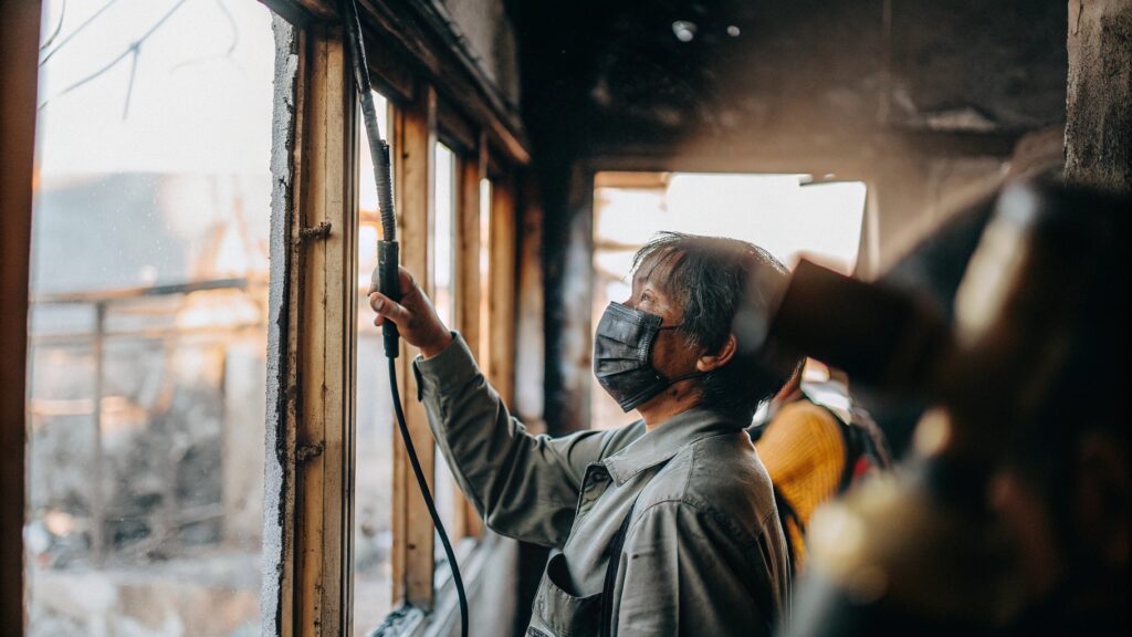 Person wearing a protective mask cleaning or inspecting a damaged building interior after a fire.