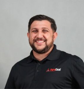 A smiling man in a black polo shirt with the PureClear logo, standing against a gray background.