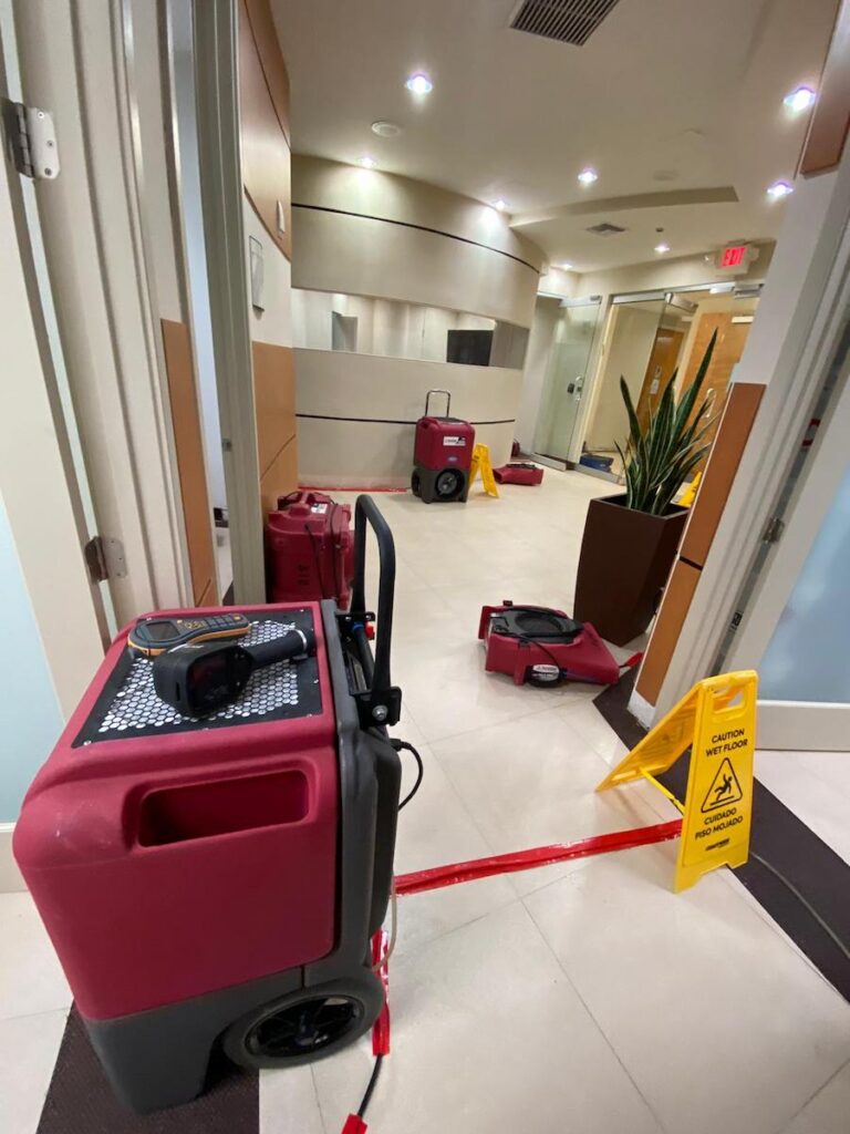 Water restoration equipment and caution signs in a hallway of a commercial building.