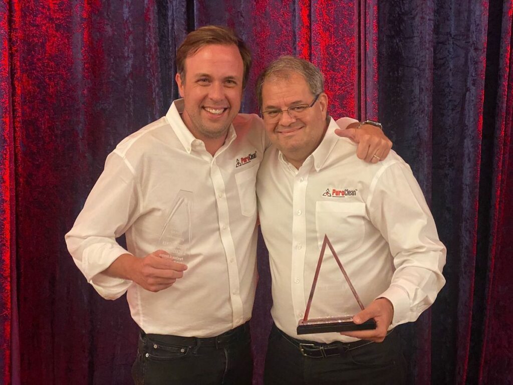 Two smiling PureClean employees proudly display their awards at a company event.