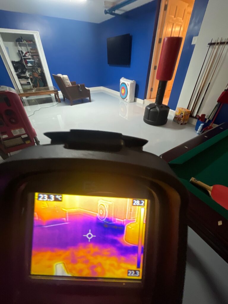 Thermal camera view showing temperature variations in a flooded basement with furniture and sports equipment.