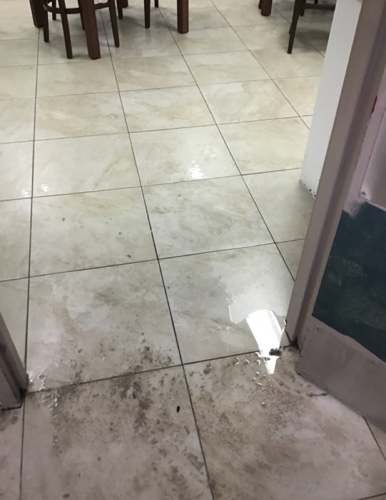 A grimy, wet tiled floor with a puddle of water near a doorway and chair legs
