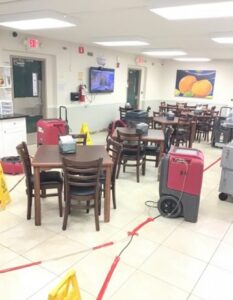 A dining room is undergoing water damage restoration with industrial drying equipment and safety cones. TITLE