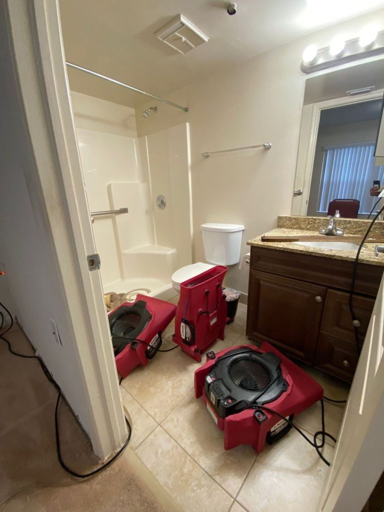 A bathroom undergoing water damage restoration with three red air movers on the tiled floor.