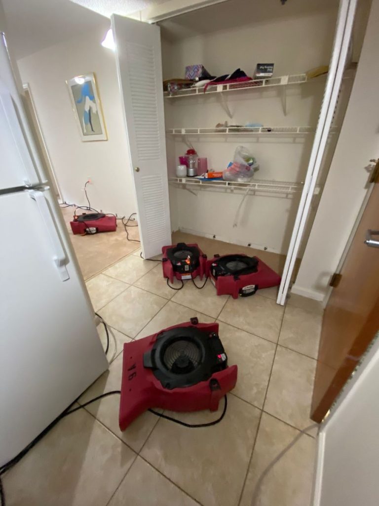 Red industrial air movers are drying tiled and carpeted floors in a room with an open