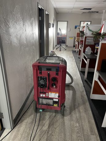 A large red water damage restoration machine operates in a modern office hallway.
