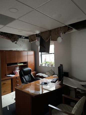 A damaged office features a partially collapsed ceiling and debris scattered across the desk.