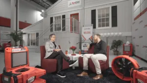 PuroClean representatives discuss services in a branded studio featuring restoration equipment and a house facade. TITLE