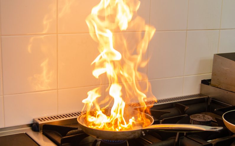 Flames erupt from a frying pan on a stove, highlighting the dangers of kitchen fires.