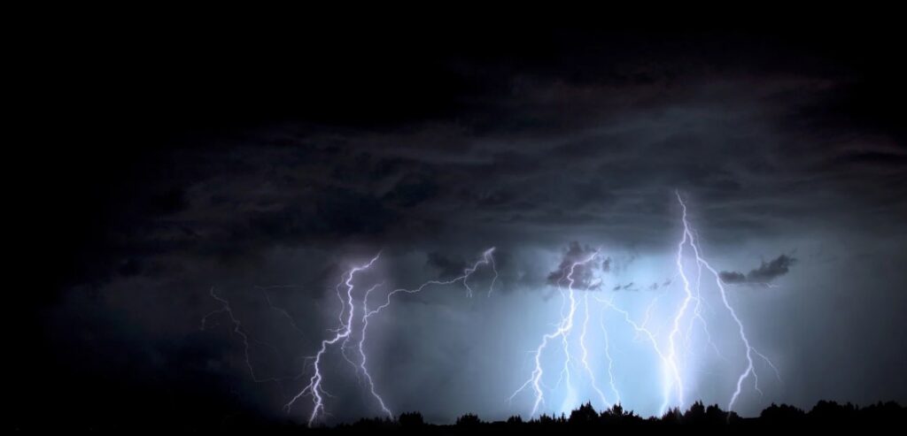 Dark storm clouds illuminated by multiple lightning strikes in a dramatic night sky.
