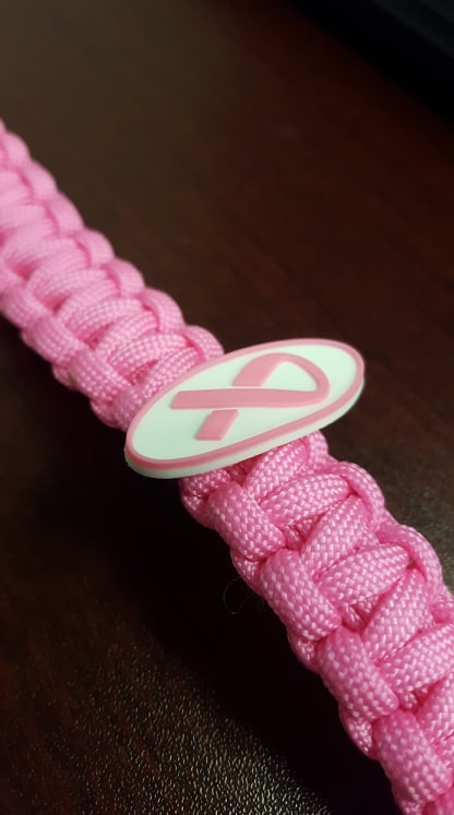 A pink paracord bracelet featuring a white ribbon symbol for breast cancer awareness.