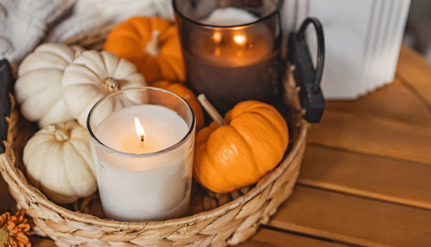 A decorative basket with white and orange pumpkins, and lit candles, set on a wooden surface for Thanksgiving.
