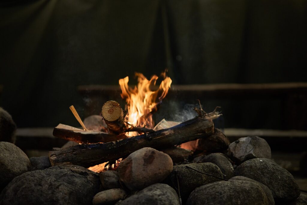 A campfire surrounded by rocks, with flames rising, set in a family-friendly camping environment.