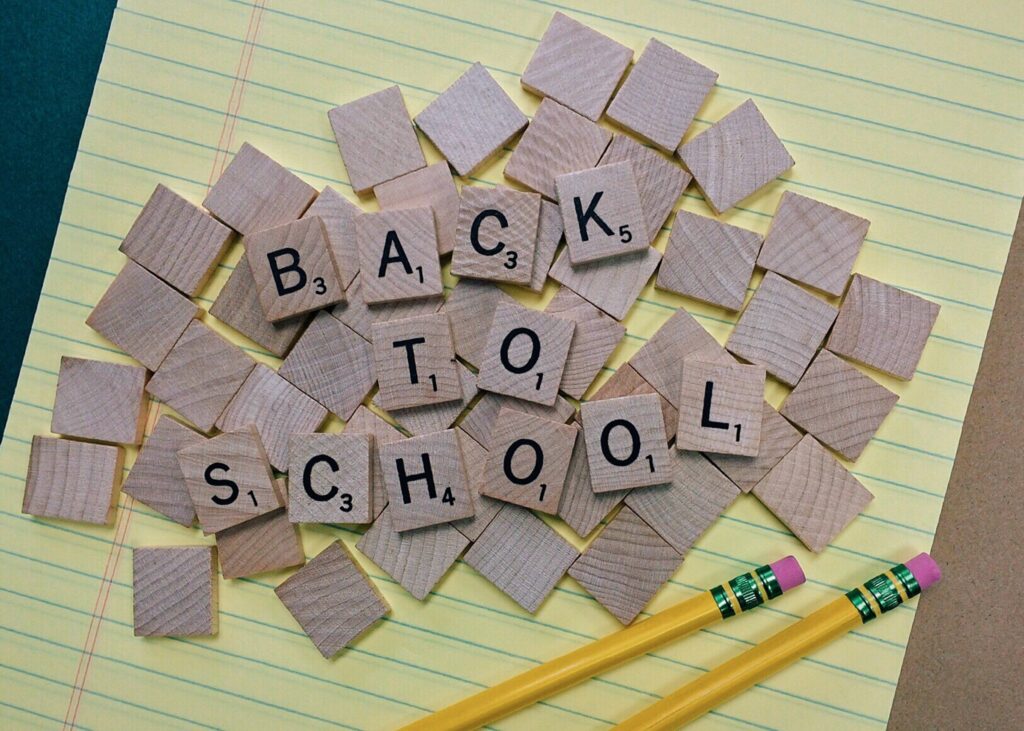 Wooden letter tiles spell "BACK TO SCHOOL" on a lined notepad with two yellow pencils.
