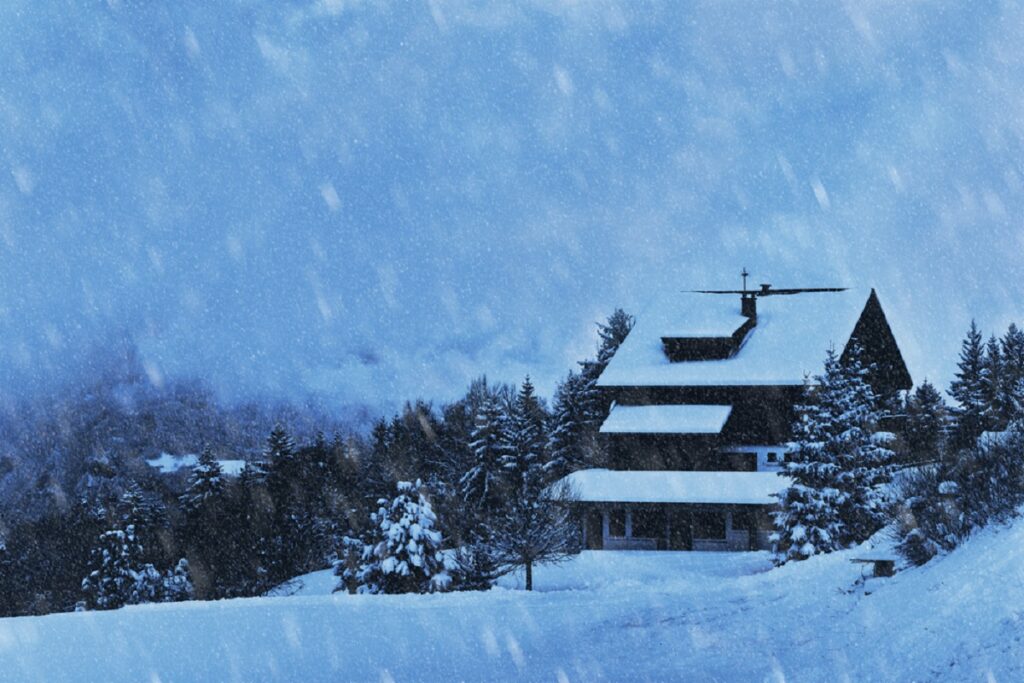 A snowy landscape featuring a house surrounded by trees during a winter storm.