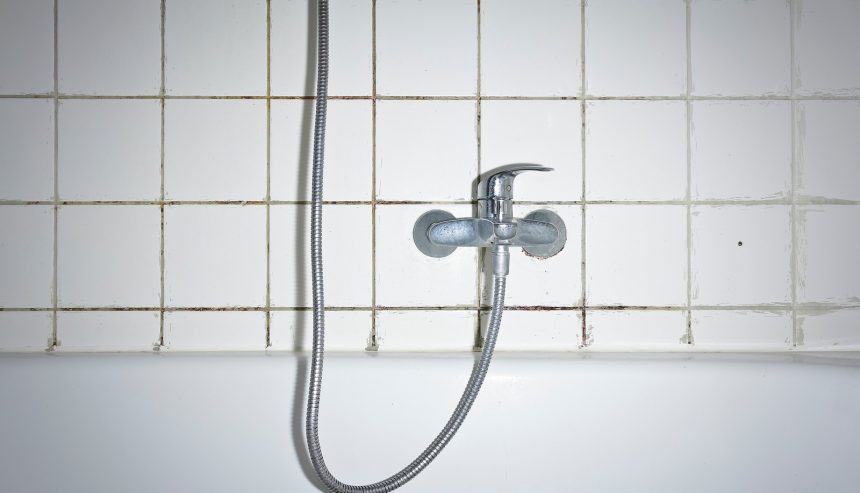 Shower faucet and tiled wall with visible mold on the grout between tiles.