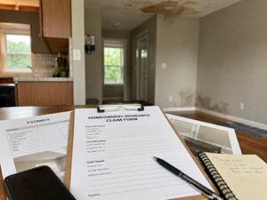 Homeowners insurance claim forms and notes on a table, with a water-damaged