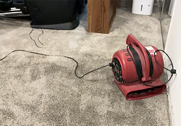 A red air mover with a black cord is drying a gray carpet