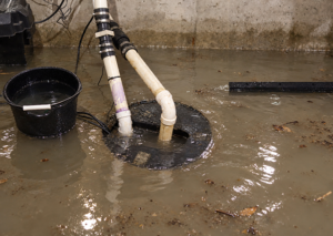 An active sump pump is surrounded by dirty floodwater and debris on a concrete basement floor