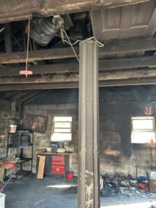 Thick soot and smoke damage covering a support beam, ceiling, and concrete block walls inside a garage after a fire.