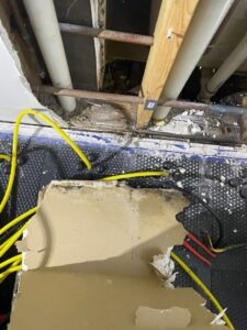 Exposed wall cavity and structural damage with mold growth, debris, and tools showing extensive water damage in a building interior.