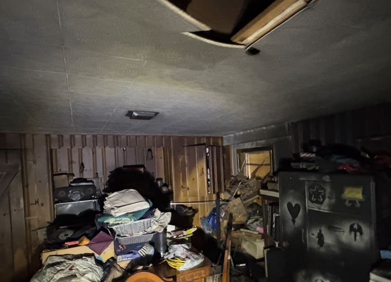 Damaged ceiling and soot-covered room showing heavy smoke damage and fire aftermath in a cluttered basement or attic.
